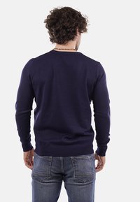 Maglione lavorato a maglia blu navy con maniche lunghe, polsini e fondo a costine. Cuciture a contrasto alle cuciture delle spalle, superficie liscia, design aderente.