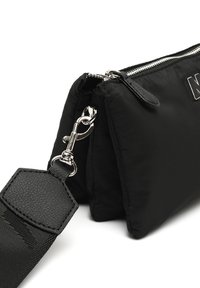 Czarna nylonowa torebka z teksturowanym skórzanym paskiem. Wyposażona w srebrne akcesoria, zamek błyskawiczny i pikowany wzór. Kompaktowy prostokątny kształt.
