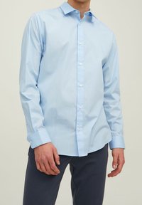Light blue button-up shirt made of smooth fabric, featuring a classic collar, long sleeves, and visible buttons along the front.