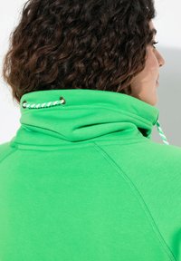 Felpa verde con colletto alto, caratterizzata da un cordino con dettagli bianchi e verdi. Texture liscia e maniche raglan.