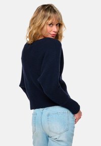 Dunkelblauer Strickpullover mit lockerer Passform, gerippten Bündchen und Saum. Kombiniert mit hellblauer Jeans im klassischen Schnitt.