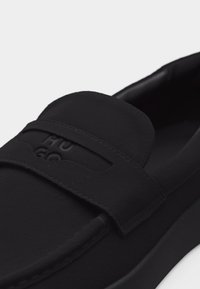 Μαύρο μοκασίνι από σουέντ με ραμμένη λωρίδα στο πάνω μέρος που φέρει ανάγλυφη επωνυμία «HUGO», με λείο στρογγυλεμένο δάκτυλο και επενδυμένη εσωτερική επένδυση.