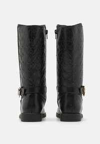 Bottes noires en simili cuir arrivant au genou, avec un motif en cœur texturé, des zips sur les côtés et une sangle décorative à boucle. Design à semelle plate.