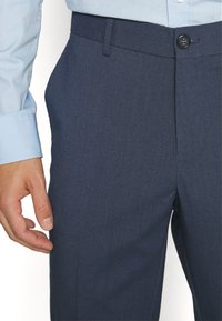 Marineblaue Anzughose aus einem glatten Stoff, mit geradem Schnitt, Knopfverschluss und seitlichen Taschen, kombiniert mit einem hellblauen Langarmhemd.