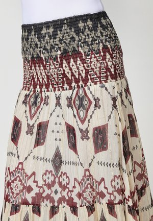 Jupe midi plissée avec taille smockée, présentant des motifs géométriques noir et bordeaux sur un fond crème. Tissu léger et texturé avec des accents dorés.