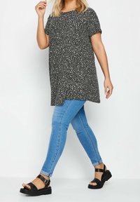 Svart och vit prickig tunika skjorta ihop med blå skinny jeans och svarta sandaler. Har korta ärmar och en avslappnad passform.