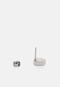 Pendientes de metal con forma hexagonal y un largo vástago. La superficie está pulida con una textura brillante y suave.