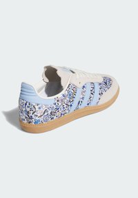 Hellfarbene Sneaker mit blauem Blumenmuster, Obermaterial aus Wildleder und Textil, Schnürverschluss, drei blaue Streifen und Gummisohle.