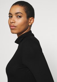 Black turtleneck top with long sleeves, made of smooth fabric. The fit is form-fitting, highlighting the neckline and shoulders.