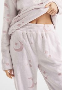 Conjunto de loungewear de felpa en rosa claro, con patrones celestiales de lunas y estrellas, cinturilla elástica y una tela suave y texturizada.