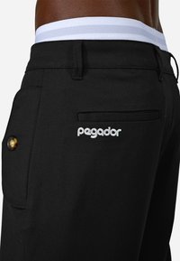 Melni bikses ar struktūru, kurām ir balta josta ar divām svītrām, zelta poga un izšūts "pegador" logo.