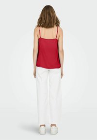 Haut à fines bretelles rouge associé à un pantalon blanc à jambes larges. Le haut présente une texture lisse, tandis que le pantalon offre une coupe structurée et ample.