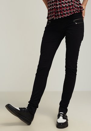 Sorte skinny jeans med lynlåslommer, let strækbart stof og en glat tekstur. Matchet med sort og hvide sko.