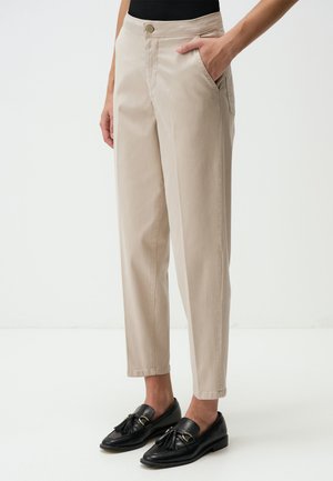Beige tailored trousers with side pockets, tapered fit, and a button closure at the waist, paired with black loafers featuring tassel accents.