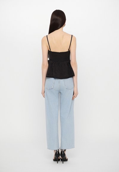 Black peplum top with thin straps, textured fabric, and ruched bodice; paired with light blue high-waisted straight-leg jeans and black heels.