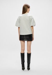 Halluxhõbedane sädelev ülisoe pluus lühikeste, puhvlike varrukatega, kombineeritud musta nahast mini-seelikuga ja põlvini ulatuvate mustade saapatega. Lihtne, moodsate joontega siluett.