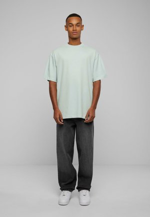 Tricou oversized de culoare verde deschis, cu mâneci scurte, asortat cu pantaloni gri închis și adidași albi. Design simplu, fără modele sau accente vizibile.