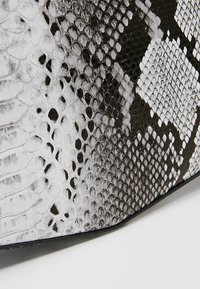 Schwarz-weißer Schlangenhautmuster mit glänzender Textur, das eine Mischung aus Schuppen in unterschiedlichen Größen und eckigen Designdetails aufweist.