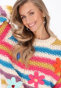 Sweter z dzianiny z żywymi paskami w kolorach różowym, niebieskim, żółtym i kremowym, ozdobiony kolorowymi aplikacjami kwiatowymi.