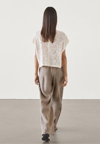 Top en dentelle crème avec une coupe décontractée et des manches courtes, associé à un pantalon marron clair. Les deux vêtements ont une apparence douce et texturée.