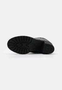 Svart boot såle med et teksturert gummidesign. Har dype spor og flere kryssmønstre for bedre grep og trekkraft.