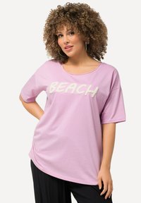 Lys pink, kortærmet t-shirt med bred udskæring og fluffy "BEACH" bogstaver på forsiden. Blødt stof, afslappet pasform og lige kant.