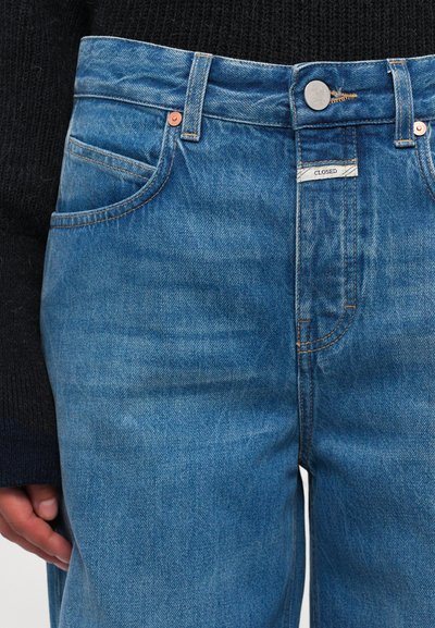 Lichtblauwe spijkerbroeken hebben een klassiek vijf-pocketontwerp, koperen klinknagels en een bedrukte label op de tailleband.