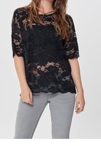 Schwarzes Spitzenoberteil mit Blumenmuster, lockere Passform, kurze Ärmel und gewellte Saum. Kombiniert mit hellgrauen Jeans für den Kontrast.