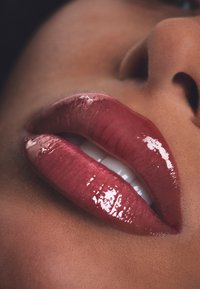 Błyszczący, głęboki różany produkt do ust o gładkiej konsystencji. Górna i dolna warga ukazują naturalną krzywiznę i połysk na neutralnym odcieniu skóry.