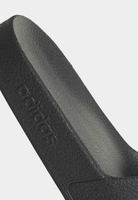 Czarny klapek z teksturowaną powierzchnią zewnętrzną, gładką wewnętrzną wkładką oraz wyraźnym logo Adidas. Prosty, wyprofilowany kształt dla komfortu.