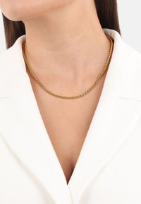 Collar de cadena trenzada de oro que se ajusta cerca del cuello, con una textura suave y un sutil brillo sobre un fondo de prenda blanca.