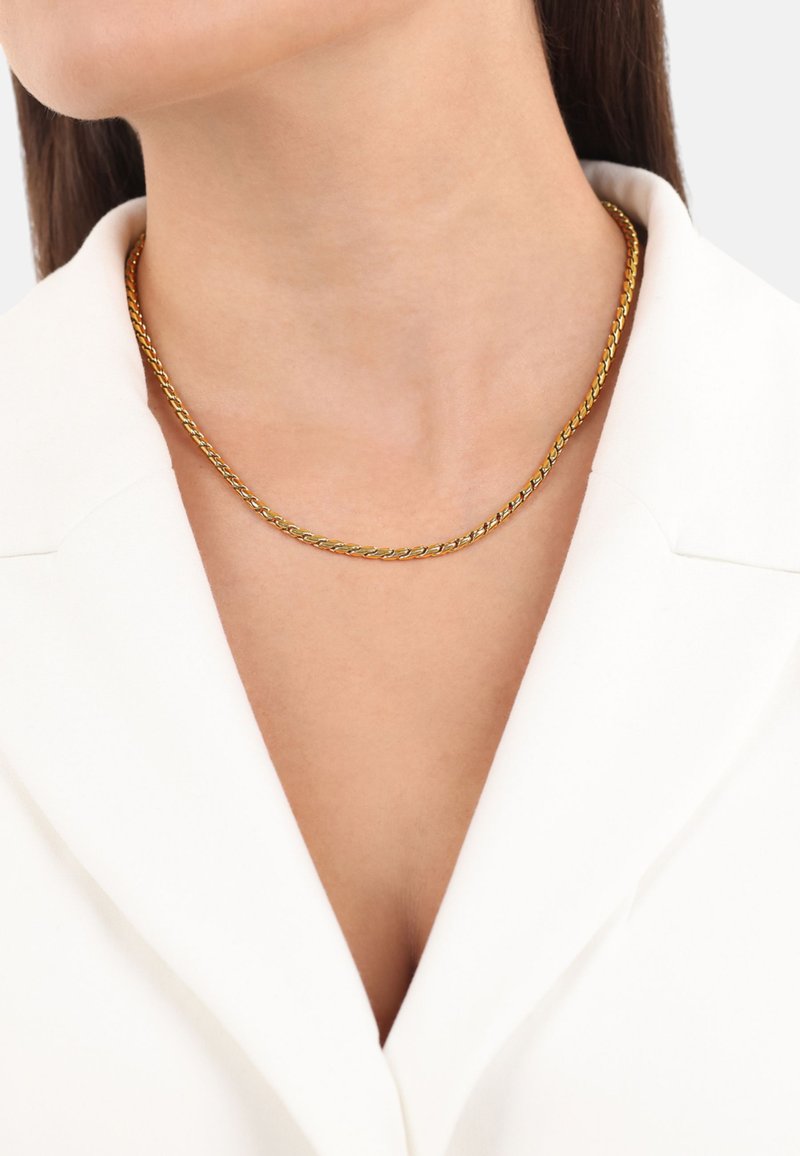 Collar de cadena trenzada de oro que se ajusta cerca del cuello, con una textura suave y un sutil brillo sobre un fondo de prenda blanca.