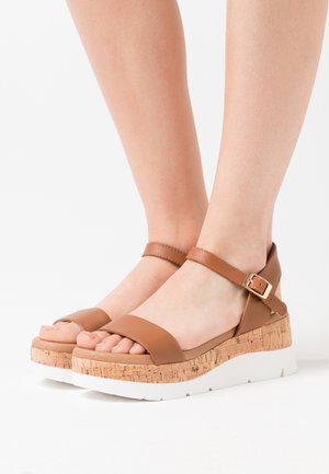 Sandales à plateforme marron avec texture en liège, large bride avant et bride de cheville réglable. Semelle extérieure blanche avec une légère courbure.