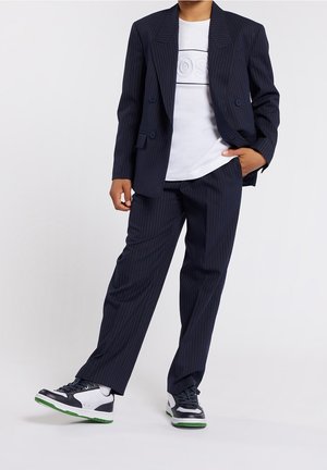 Traje de rayas navy con una chaqueta de doble botonadura y pantalones a juego, combinado con una camiseta blanca de cuello redondo y zapatillas deportivas.