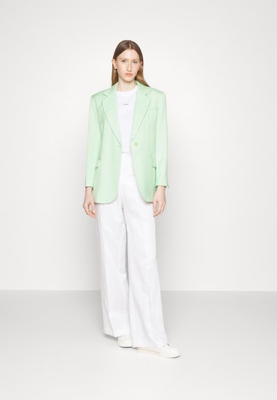 Blazer vert menthe avec des revers, fermeture à un bouton et deux poches, associé à un haut blanc et un pantalon large blanc.
