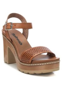 Sandalias de plataforma de cuero marrón con una correa perforada, hebilla ajustable en el tobillo y un tacón grueso. Suela de color claro y acentos de costura.