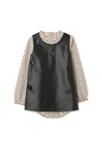 Schwarzes Kunstleder-Kleid ohne Ärmel mit gestickten Herzdetails über einer langärmligen cremefarbenen Bluse mit kleinen Herzmotiven und pinken Rüschensäumen.