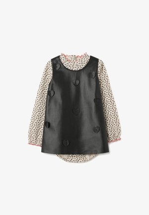 Black faux leather sleeveless dress with stitched heart details over long-sleeve cream blouse with small heart print and pink ruffled cuffs.