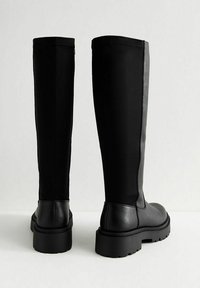 Kniehoge zwarte laarzen met een glad leren neus en een robuuste zool, voorzien van een contrasterend stoffen paneel aan de achterkant. Matte afwerking.