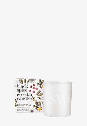 Bougie cylindrique blanche avec "thisworks" en relief. Accompagnée d'une boîte décorative ornée de motifs floraux et comportant le texte "épices noires et cèdre".