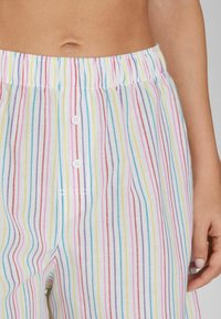 Pruhované kalhoty z lehkého materiálu s barevnými svislými pruhy (růžová, modrá, žlutá) a elastickým pasem se detailním knoflíkem.