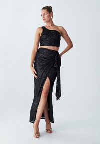 Black sequined two-piece outfit featuring a one-shoulder crop top and a high-slit skirt, tied at the waist with a bow.