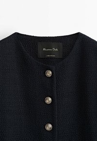 Laivastonsininen teksturoitu bleiseri pyöreällä kaula-aukolla, jossa on kolme koristeellista hopeanappia ja musta etiketti, jossa lukee "Massimo Dutti".