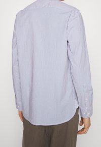 Chemise à manches longues rayée bleu clair et blanche, avec un ourlet incurvé, des poignets à boutons et un col classique. Matériau en coton.