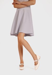 Gonna svasata grigia in tessuto morbido. Modella che indossa scarpe Mary Jane in pelle laccata rosa pallido con dettagli a fibbia.