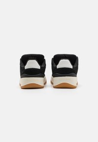 Sorte semskete og syntetiske sneakers med hvite helkontakter og beige mellomsåler. Lysebrune gummisåler. "TOMMY JEANS" preget på baksiden.