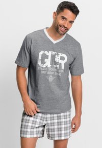 Graues Kurzarm-T-Shirt mit weißem V-Ausschnitt, mit einem abgenutzten Grafikdruck. Kombiniert mit karierten grauen Shorts, die einen lässigen Look schaffen.