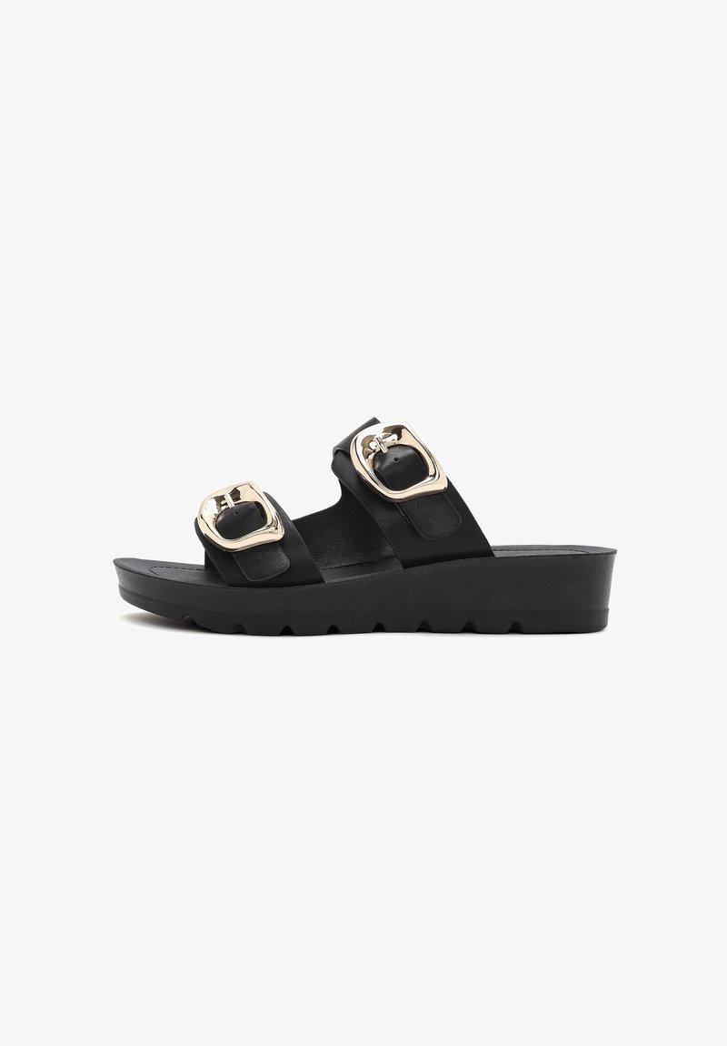 Black slide sandals feature two large silver square buckles and a textured sole. Made of smooth material with a chunky wedge design.