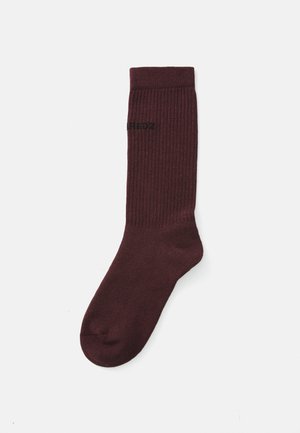 Burgundy ribbed sock made of soft fabric. Features a reinforced heel and toe, with a black printed logo near the top.