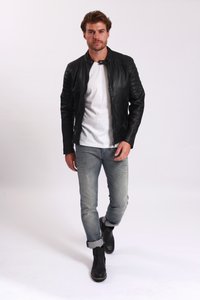 Svart läderjacka med ribbade axlar, bärs över en vit skjorta, i kombination med ljusblå slitna jeans och svarta ankelboots.